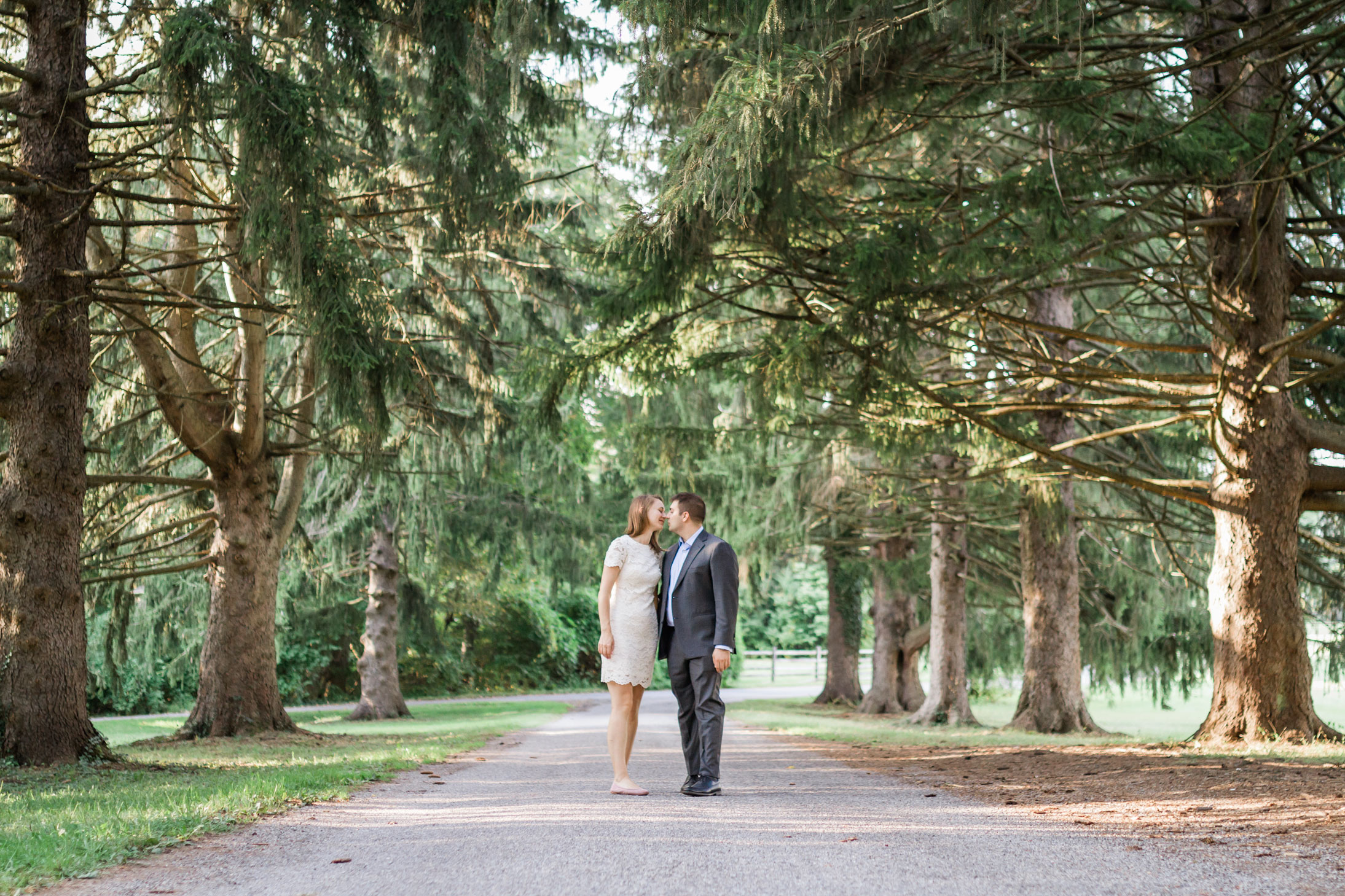 couple strolling through the park with evergreen trees surrounding them 